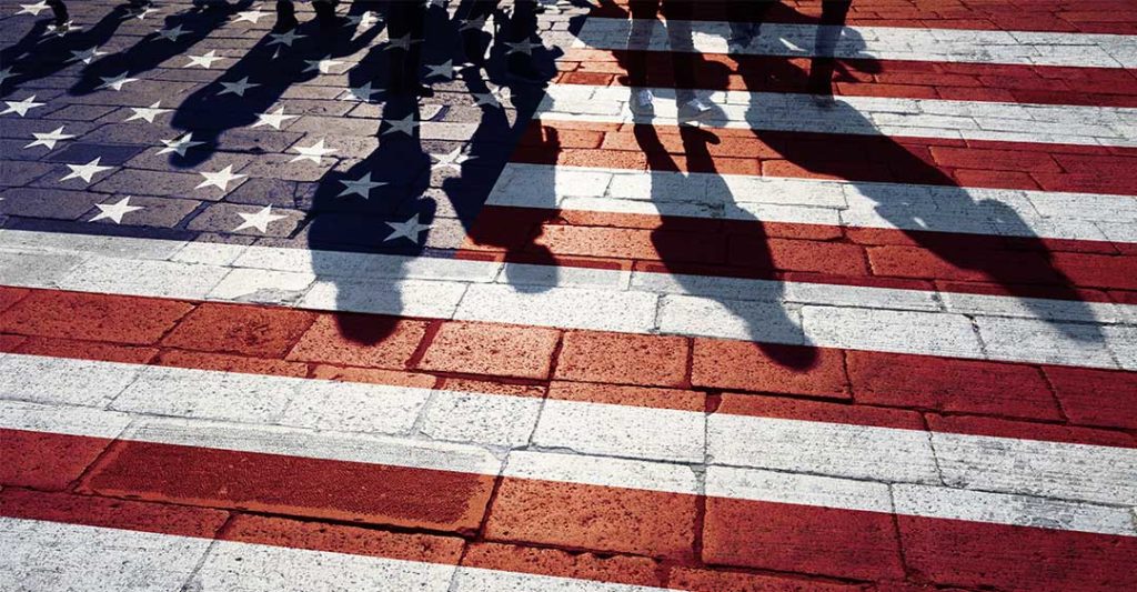 drapeau américain peint sur une allée en briques avec des ombres de personnes marchant, les règles d'immigration de Biden, ont un impact sur les entreprises, commerce international