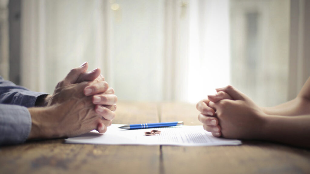 Vue de mains, mari et femme avec des alliances, document et stylo sur une table, divorce d'un propriétaire d'entreprise