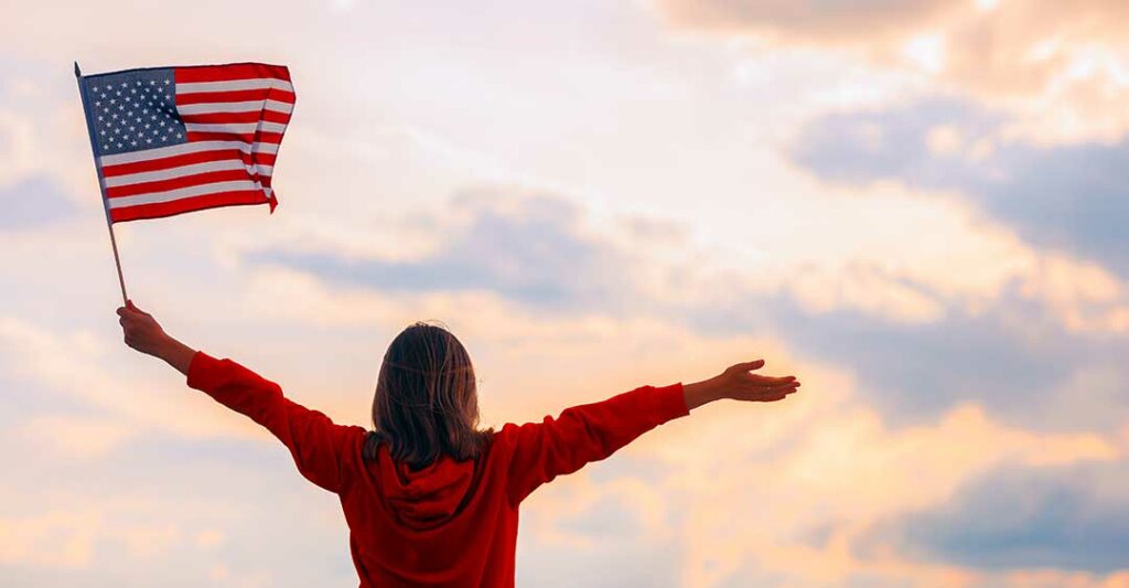 femme tenant le drapeau américain et regardant le ciel avec les bras ouverts, avocate de la citoyenneté