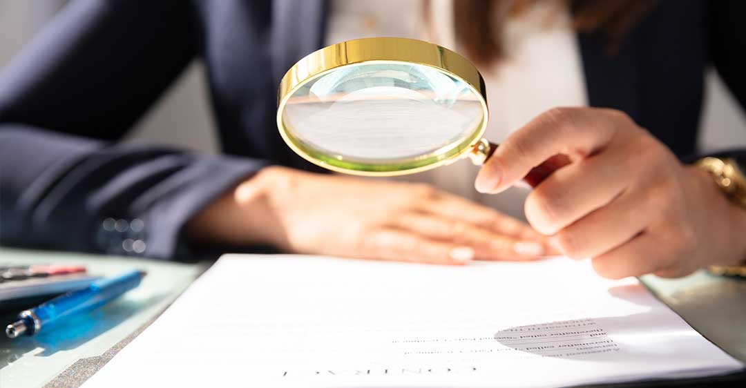 femme d'affaires avec une loupe, regardant un document, pourquoi les fautes de frappe et de grammaire dans un contrat peuvent être désastreuses